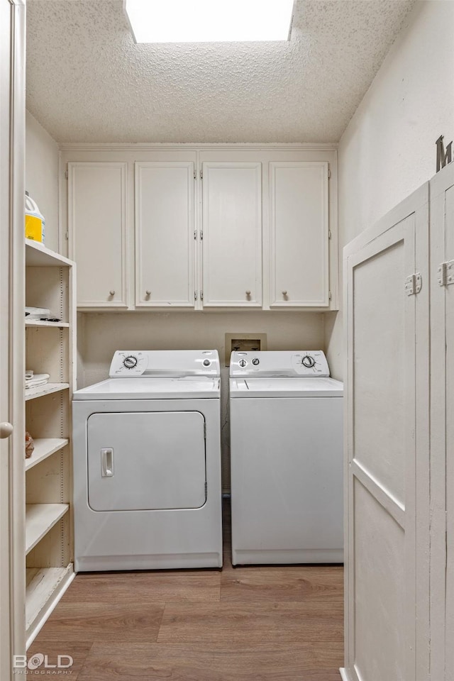 clothes washing area with light wood-type flooring, a textured ceiling, cabinet space, and washing machine and clothes dryer
