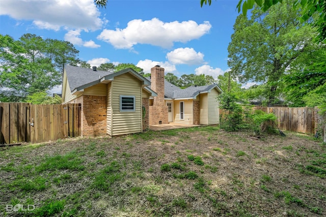 rear view of house featuring a fenced backyard, roof with shingles, a chimney, brick siding, and a patio area