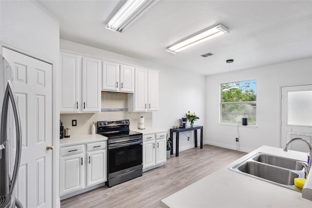 kitchen with appliances with stainless steel finishes, a sink, light wood finished floors, white cabinetry, and tasteful backsplash