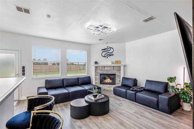 living area featuring a brick fireplace, a textured ceiling, visible vents, and wood finished floors