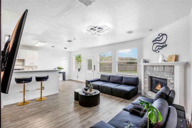 living area featuring visible vents, a textured ceiling, light wood finished floors, and a brick fireplace