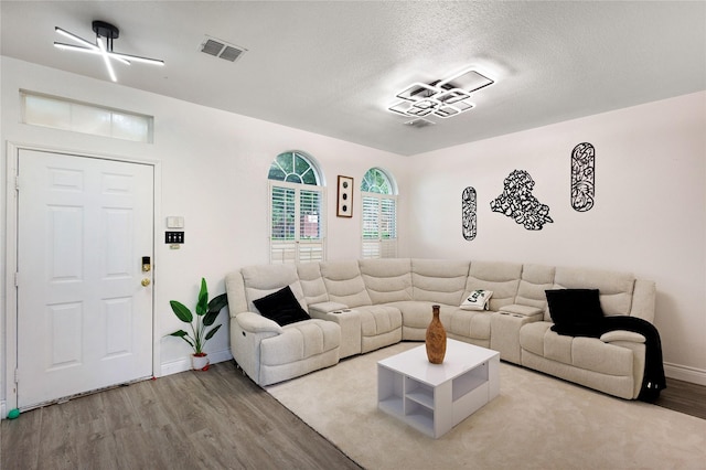 living room featuring a textured ceiling, baseboards, visible vents, and wood finished floors