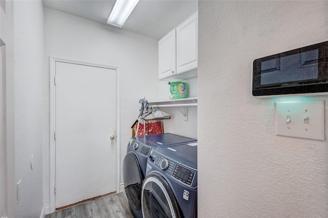 clothes washing area with a textured wall, cabinet space, washing machine and dryer, and light wood-style flooring