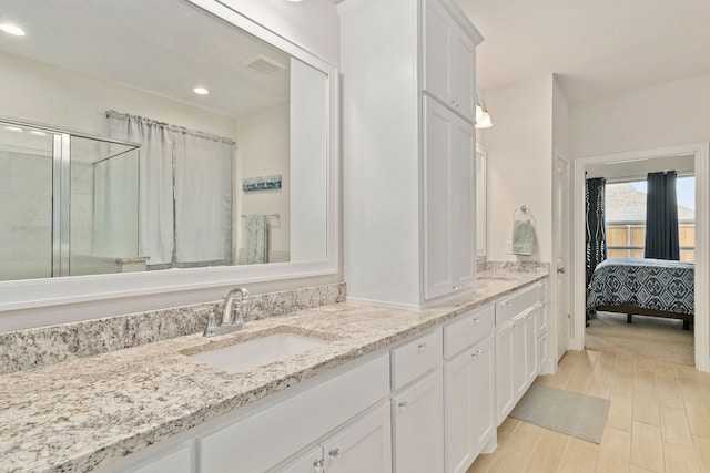 ensuite bathroom with double vanity, wood finished floors, recessed lighting, a sink, and a stall shower