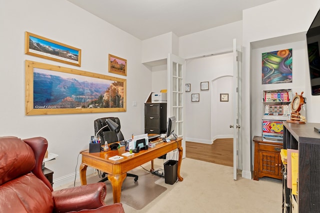 office area featuring baseboards and light carpet