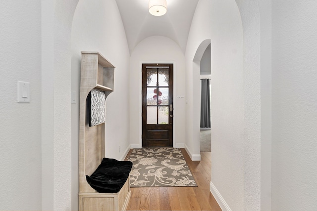 doorway featuring arched walkways, baseboards, vaulted ceiling, and light wood-style flooring