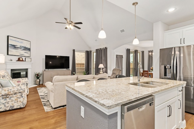 kitchen featuring a center island with sink, a sink, light wood finished floors, open floor plan, and stainless steel appliances