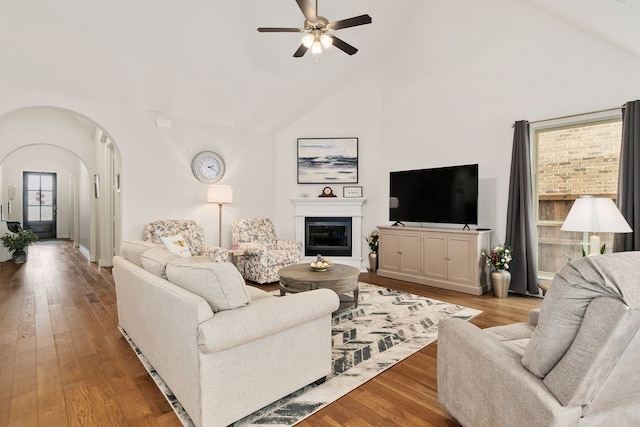 living room with a ceiling fan, high vaulted ceiling, wood finished floors, and arched walkways