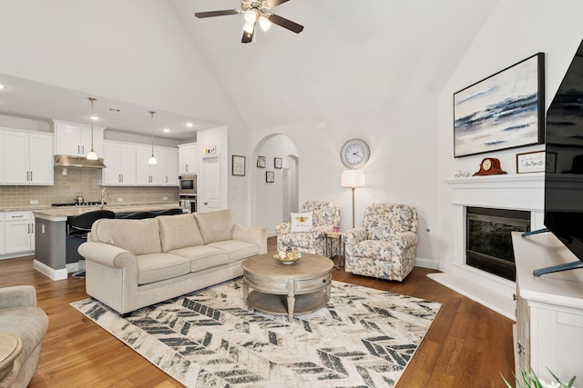 living area with a glass covered fireplace, arched walkways, ceiling fan, and wood finished floors