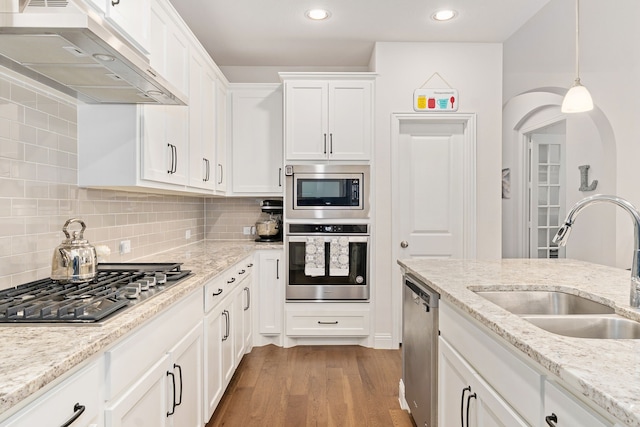 kitchen featuring wood finished floors, white cabinetry, under cabinet range hood, a sink, and appliances with stainless steel finishes