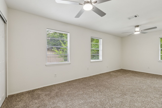 empty room with visible vents, a ceiling fan, carpet flooring, and a wealth of natural light
