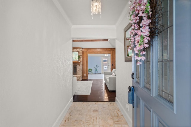 foyer entrance with crown molding, baseboards, an inviting chandelier, and a large fireplace