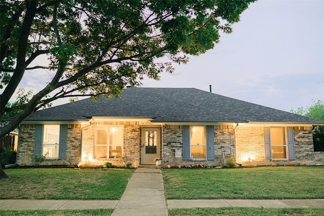 single story home with a shingled roof, a front lawn, and brick siding