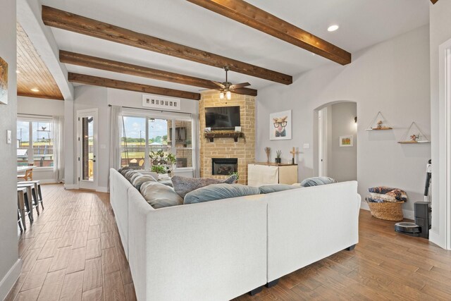 living area with a brick fireplace, arched walkways, a ceiling fan, and wood finished floors