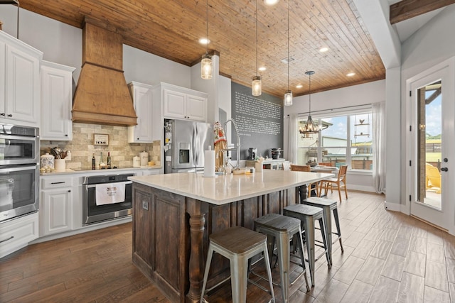 kitchen featuring wood ceiling, backsplash, a center island with sink, light countertops, and stainless steel fridge