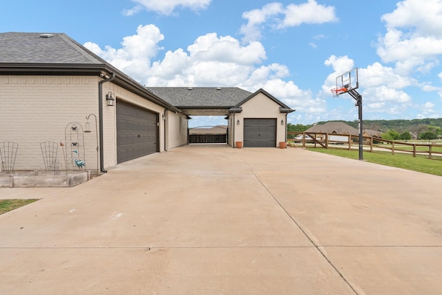 view of side of property with fence, a shingled roof, brick siding, a garage, and driveway