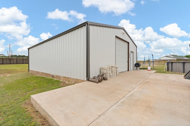 view of outdoor structure with fence, an outbuilding, and driveway
