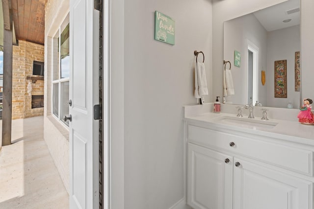 bathroom with vanity, brick wall, a stone fireplace, visible vents, and wood ceiling