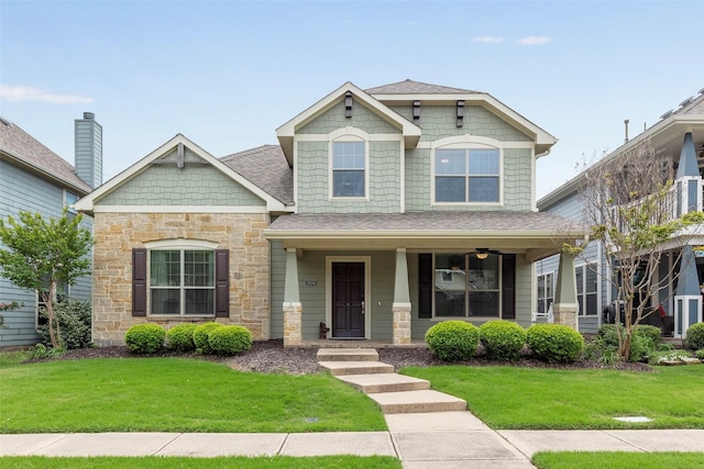 craftsman-style home featuring covered porch, a shingled roof, a front lawn, and stone siding