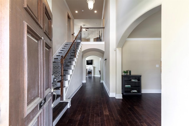 foyer entrance featuring a towering ceiling, arched walkways, dark wood finished floors, baseboards, and stairs