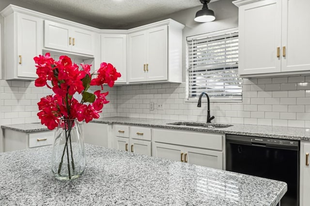 kitchen with a sink, white cabinetry, dishwasher, and light stone countertops