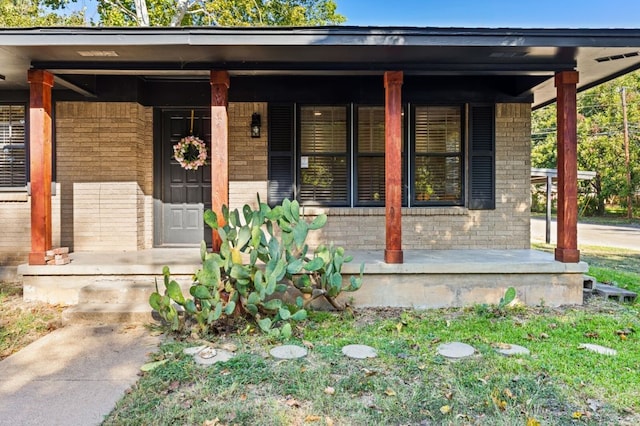 view of exterior entry with brick siding and covered porch