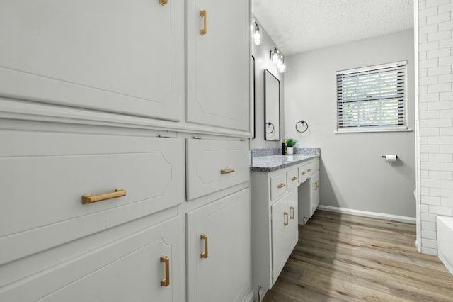 bathroom with vanity, a textured ceiling, baseboards, wood finished floors, and a tub to relax in