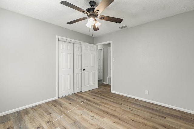 unfurnished bedroom with baseboards, visible vents, wood finished floors, and a closet