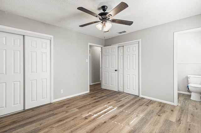 unfurnished bedroom featuring visible vents, baseboards, wood finished floors, and two closets