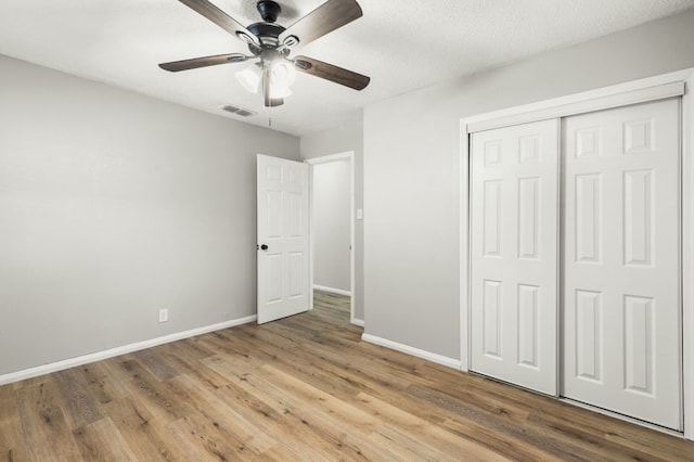 unfurnished bedroom featuring visible vents, a closet, wood finished floors, baseboards, and ceiling fan