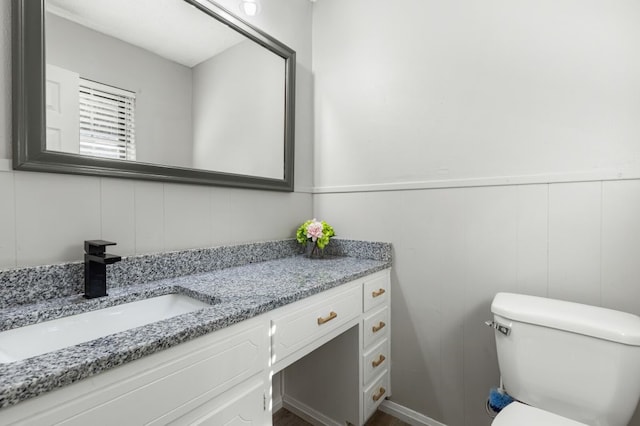 half bath featuring vanity, a wainscoted wall, a decorative wall, and toilet