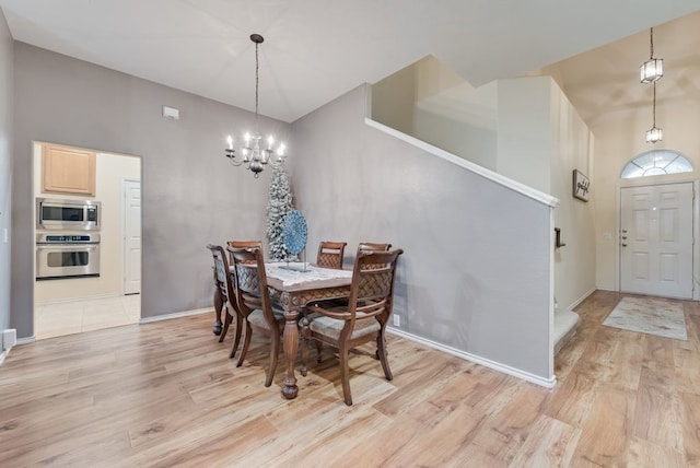 dining area featuring baseboards, a notable chandelier, a high ceiling, and light wood-type flooring