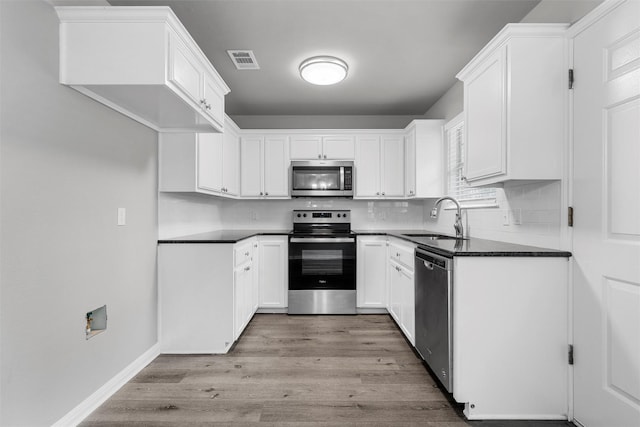 kitchen with visible vents, appliances with stainless steel finishes, dark countertops, light wood-type flooring, and a sink