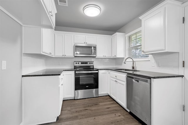 kitchen featuring white cabinets, dark countertops, appliances with stainless steel finishes, a sink, and visible vents
