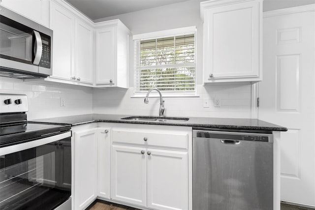 kitchen with a sink, appliances with stainless steel finishes, white cabinets, and dark stone countertops