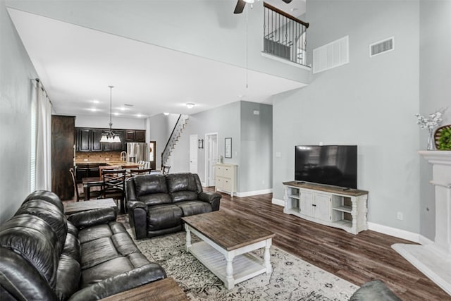 living room featuring visible vents, baseboards, ceiling fan with notable chandelier, and dark wood-style floors