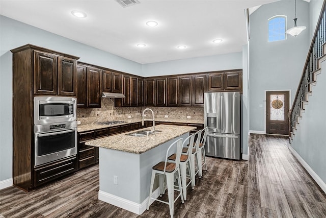 kitchen with under cabinet range hood, dark brown cabinets, appliances with stainless steel finishes, and a sink