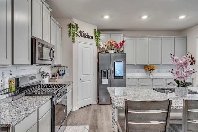 2561 Pettus Dr, Forney, TX 75126 - kitchen featuring light stone counters, a sink, stainless steel appliances, light wood-type flooring, and backsplash