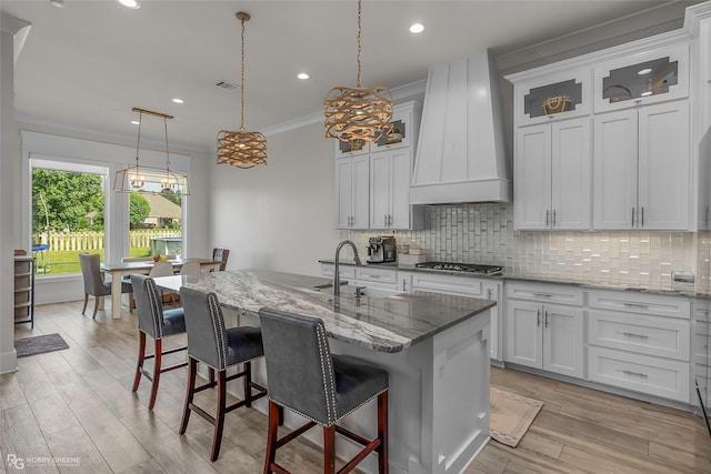 kitchen with custom exhaust hood, light wood-style flooring, stainless steel gas stovetop, tasteful backsplash, and ornamental molding