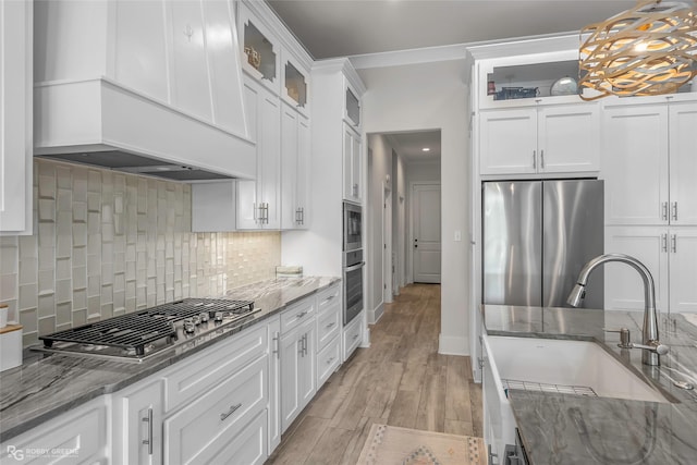 kitchen featuring a sink, premium range hood, stainless steel appliances, white cabinetry, and decorative backsplash