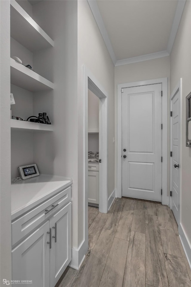 corridor with crown molding, baseboards, and light wood-type flooring