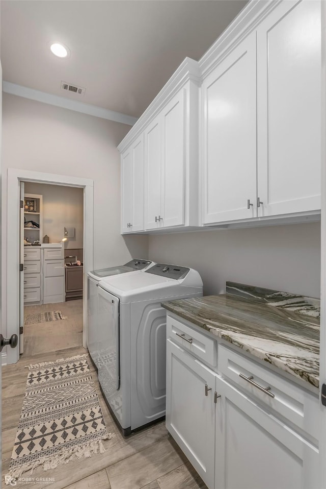 laundry area featuring visible vents, crown molding, washing machine and dryer, cabinet space, and light wood finished floors