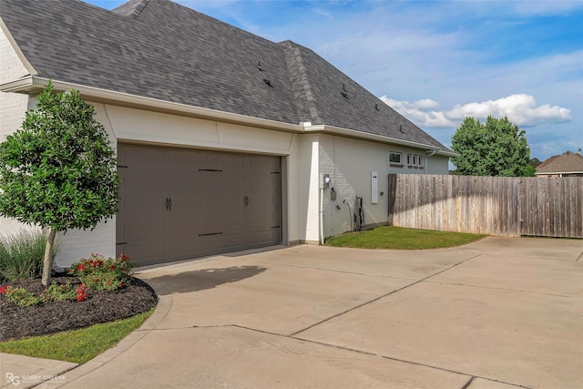 view of home's exterior with a garage, fence, concrete driveway, a shingled roof, and stucco siding