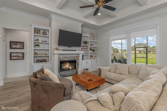 living room with a ceiling fan, a fireplace, light wood-type flooring, beam ceiling, and ornamental molding