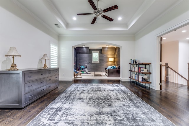 living area featuring dark wood-style flooring, ceiling fan, a raised ceiling, arched walkways, and visible vents