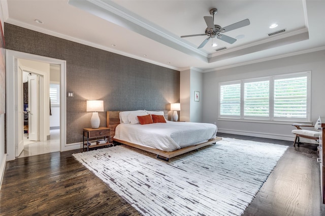 bedroom with a tray ceiling, visible vents, dark wood-style floors, and ornamental molding