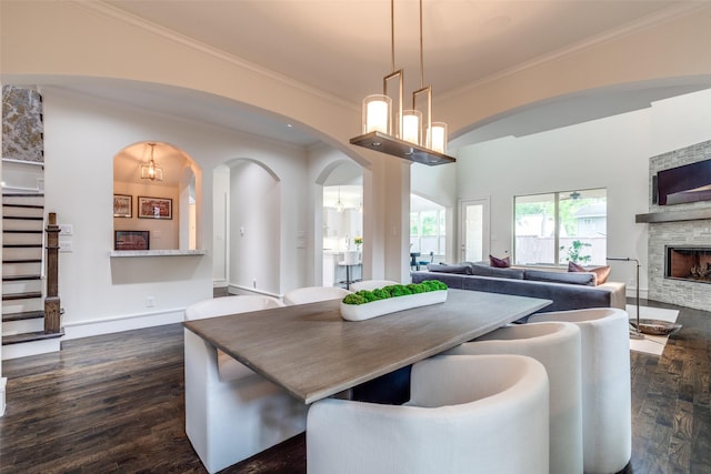 dining room featuring arched walkways, ornamental molding, a fireplace, and dark wood finished floors