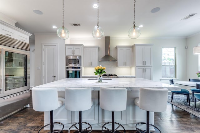 kitchen featuring ornamental molding, built in appliances, wall chimney range hood, and tasteful backsplash