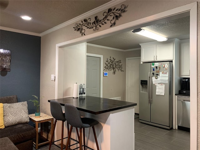 kitchen with a kitchen bar, a textured ceiling, dark countertops, appliances with stainless steel finishes, and white cabinetry