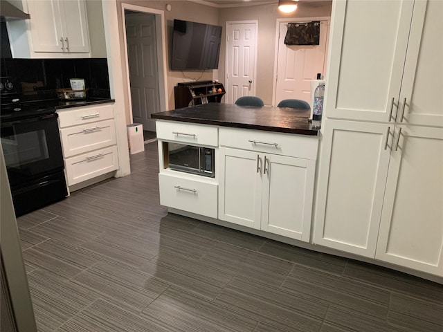 kitchen with wall chimney exhaust hood, black appliances, dark countertops, and white cabinetry